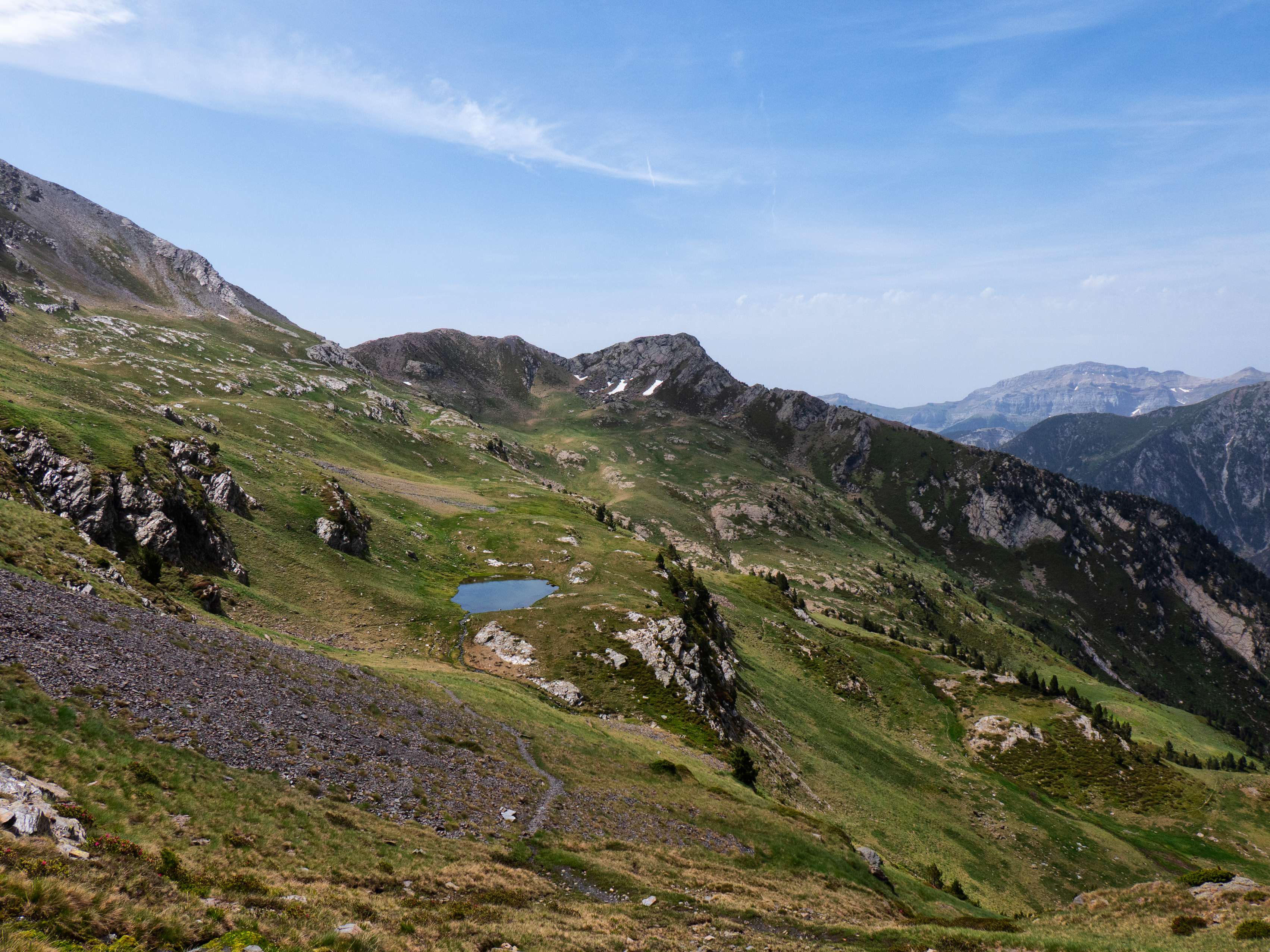 Durante esta diagonal, tenemos una perspectiva bastante completa del pequeño circo herboso de Salcorz, con los Picos del Cabo en el otro extremo y el ibón en su centro.