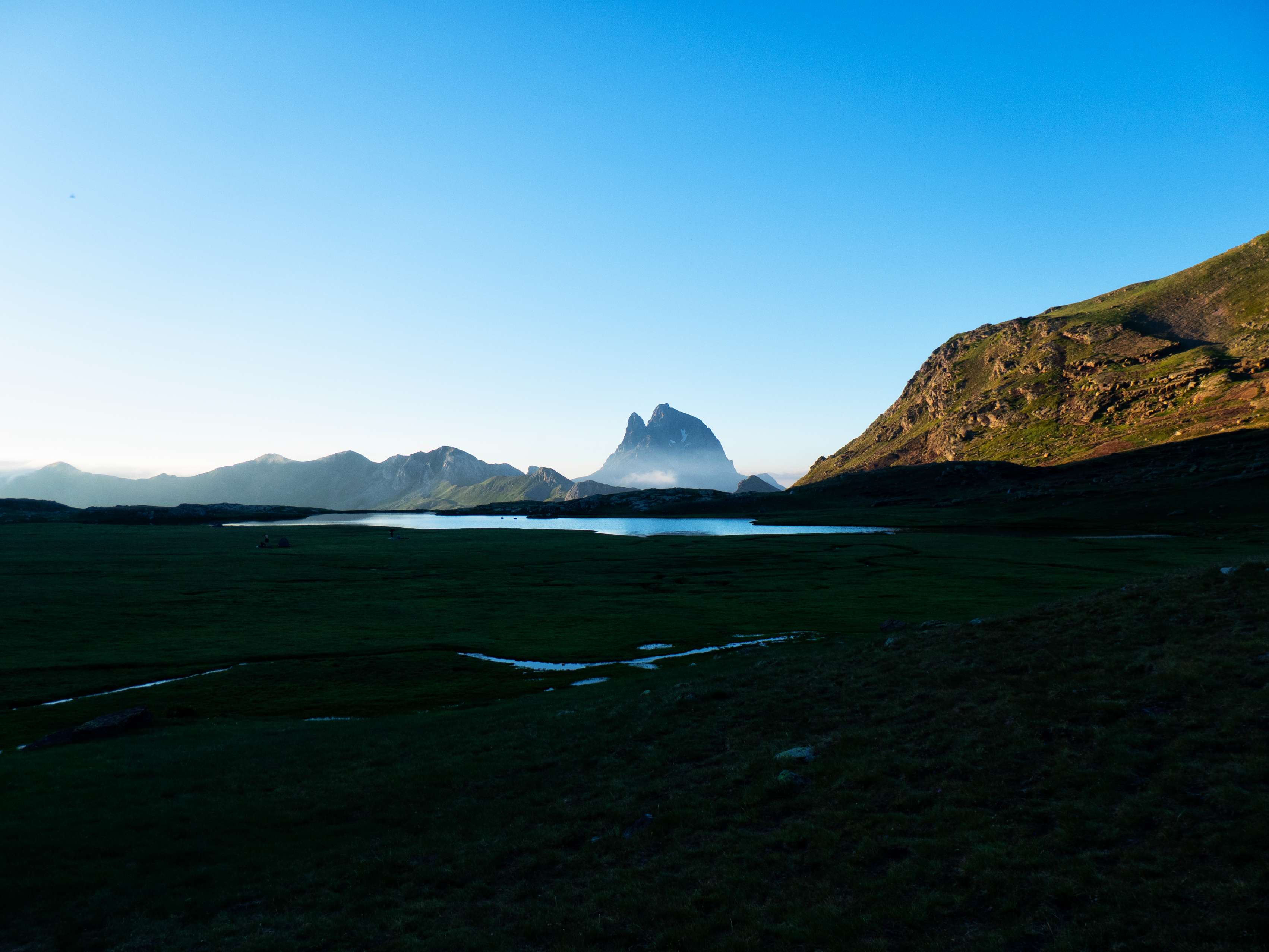 Llegamos así a los extensos Llanos de Anayet, un paraje de una belleza incomparable. Este paradisíaco lugar, encajonado entre las cimas del macizo homónimo, es un extenso rellano herboso donde confluyen las aguas que caen de las crestas del circo, que se concentran en dos ibones. Antiguamente eran tres, pero el más meridional quedó colmatado, un destino que le aguarda también al segundo de ellos, cuyo tamaño va reduciéndose poco a poco ante los sedimentos que van ocupando su mitad meridional. Sin embargo, el valor de este paraje no es menor por este hecho, más bien lo contrario, pues la colmatación del ibón transforma el terreno en turberas y humedales de alto valor ecológico.