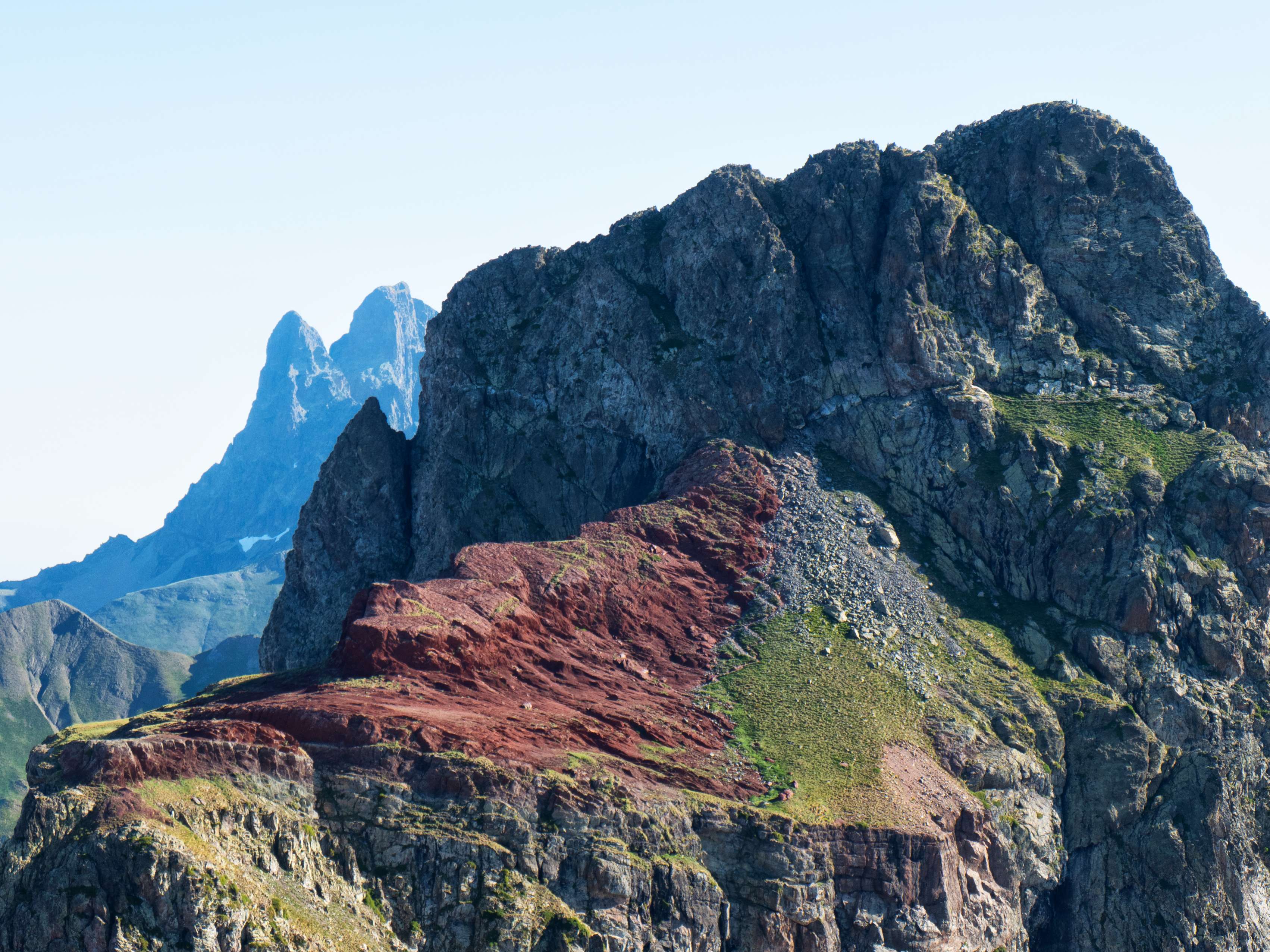 Mientras vamos avanzando por la arista, nuestra perspectiva sobre el Anayet va cambiando poco a poco, pudiendo distinguir a la perfección todo el itinerario hasta llegar a su cima: la terraza rojiza, la pedrera, el paso de las cadenas, la vira herbosa y la canal diagonal que llega a la cima, donde ahora vemos a dos personas. Además, según nos vamos desplazando, el Anayet va ocultando poco a poco la bífida forma del Midi. Los dos restos volcánicos más famosos del Pirineo, codo con codo.