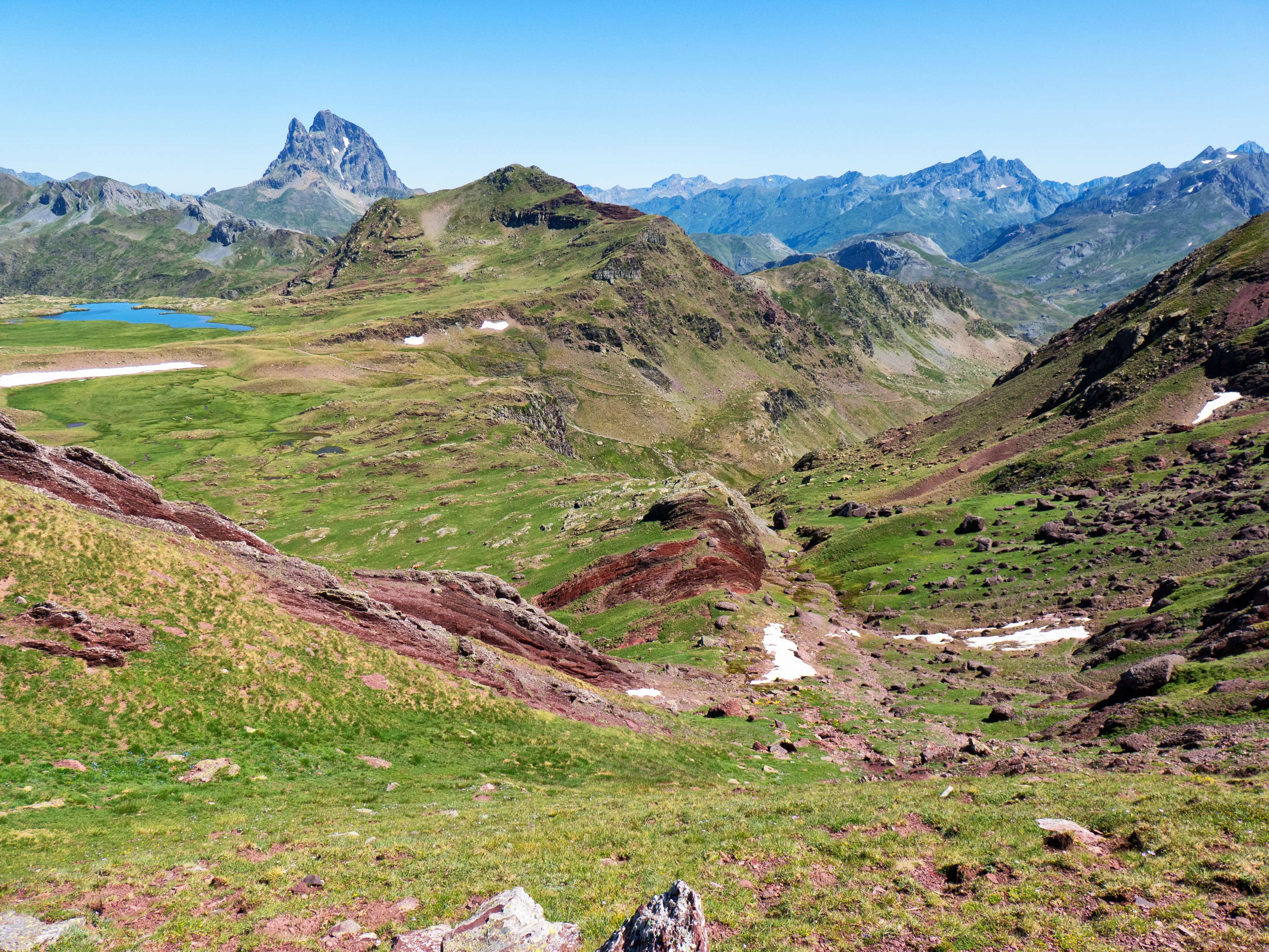 Nuestro objetivo es enlazar con el sendero que sube a los Llanos de Anayet desde la estación de Formigal, cuyo trazado vemos en el fondo del barranco. Aunque podríamos girar a la izquierda para unirnos a él cerca del ibón, es mucho más rápido descender por el tubo que vemos a la derecha de la mancha rojiza que tenemos enfrente, que nos conducirá directamente al barranco de Culivillas, donde podremos tomar el sendero en un punto más avanzado.