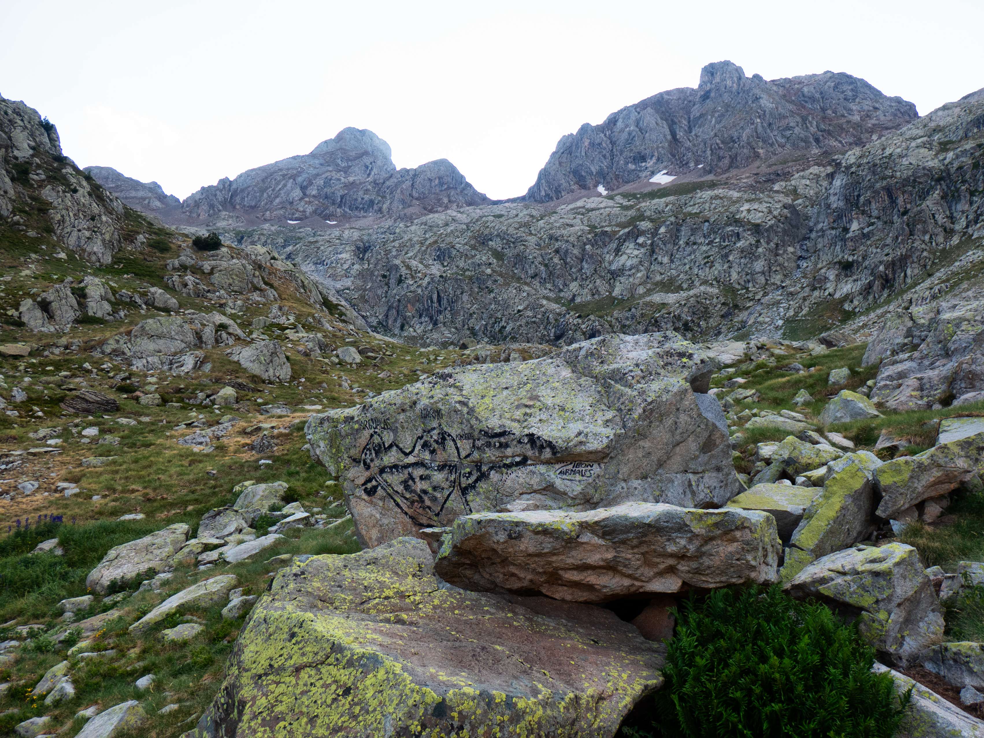 ...a esta curiosa piedra pintada, que nos ofrece una fotografía lítica de lo que vemos por encima de nosotros. Desde este punto, ya sobre los 2.200 metros de altitud, tenemos una visión diáfana de las principales cumbres que hollaremos mañana, separadas por el boquete del Collado de Argualas: el pilar rocoso del Argualas a la izquierda, y la uniforme mole del Garmo Negro, solo rota por el colmillo de la Aguja de Pondiellos, a la derecha. Y, a la derecha de esta última cumbre, el Collado de Pondiellos. En este peculiar mapa a gran escala se detalla la manera de llegar a cada uno de estos puntos. En nuestro caso, nos interesa la ruta que, avanzando con tendencia hacia la derecha, llega al Collado de Pondiellos para así empezar el itinerario de todas las cumbres de este pequeño macizo.