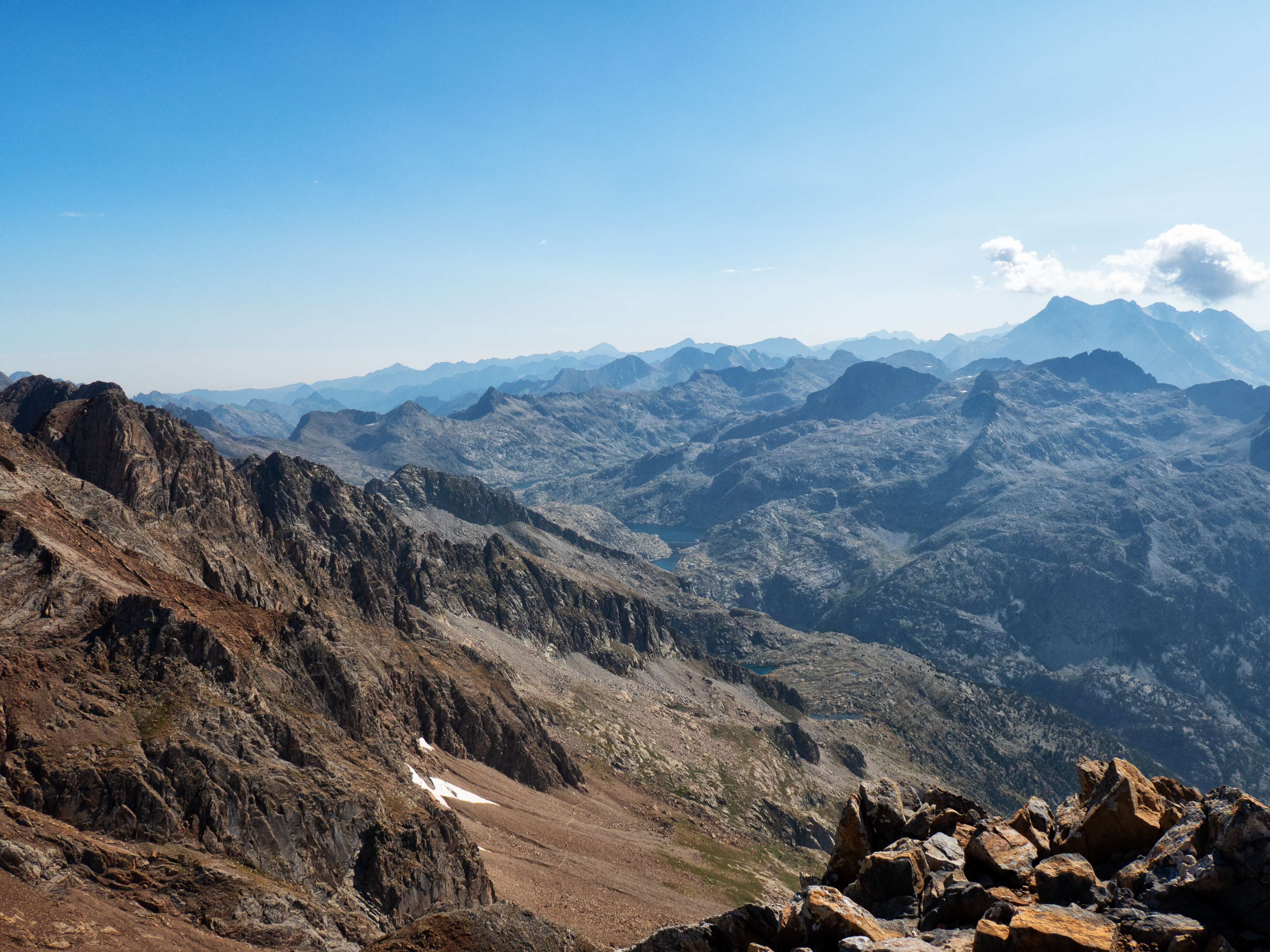 Tras las sucesivas crestas que se desprenden del cordal principal de Panticosa, vemos la extensa cuenca lacustre de Bachimaña y Bramatuero, uno de los lugares del Pirineo con mayor densidad lacustre. Y cerrando el horizonte, las mil montañas del Pirineo francés, desde el Montaigu y el Midi de Bigorre hasta las crestas del Neouvielle y el Pic Long, este último medio escondido tras la mole del Vignemale. Pero ahora nos fijamos en un punto mucho más cercano. Bajo las paredes inferiores del Garmo Negro observamos un trazo cortando la pedrera en diagonal. Este será nuestro sendero de retorno a los Baños de Panticosa, y hacia allí nos dirigiremos ahora.