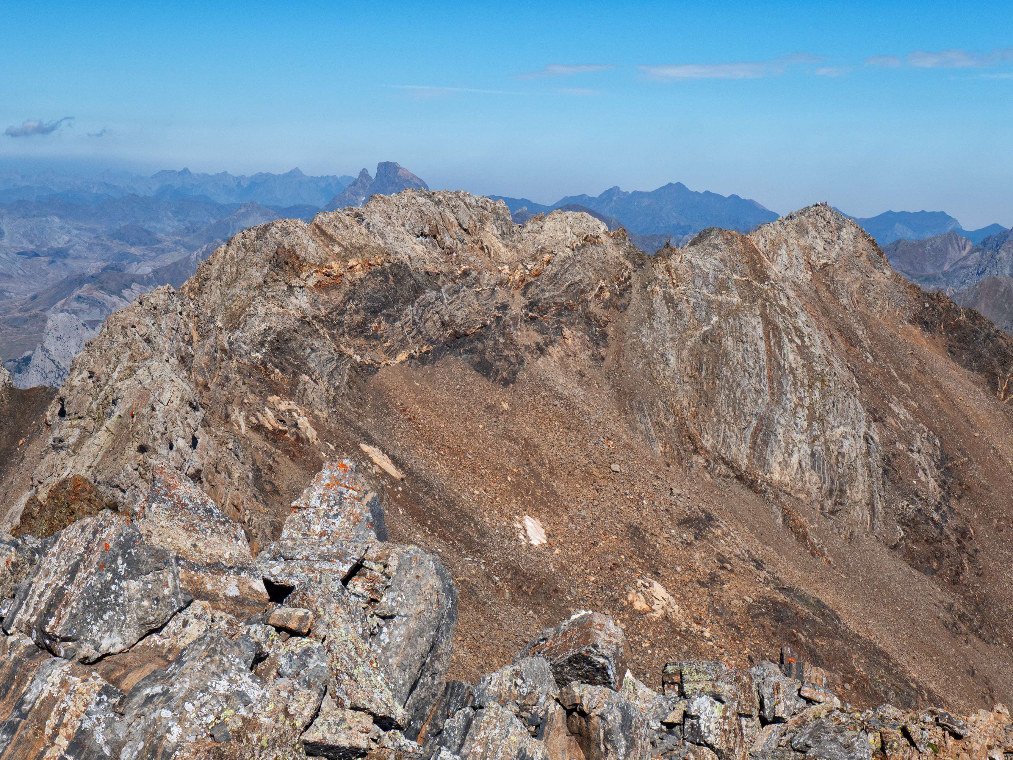 En las cimas de Algas encontramos una afluencia intermedia. Curiosamente, donde vemos a más gente es en el Algas Norte, mientras que también observamos a unos montañeros recorrer la afilada arista entre el Argualas y el Algas SE, que tiene algunos pasos de tercer grado. Y, tras la cima principal, el Midi d'Ossau y la lejana pirámide del Anie, ambas situadas íntegramente en Francia.